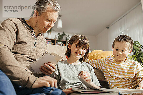 Father with happy children looking at old photo album in home