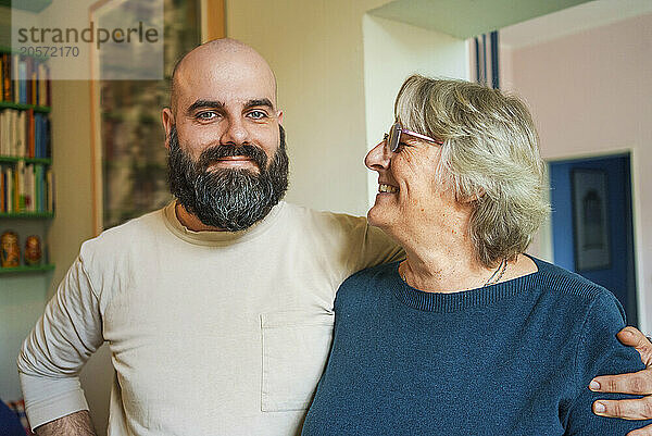 Smiling bearded man with arm around mother at home