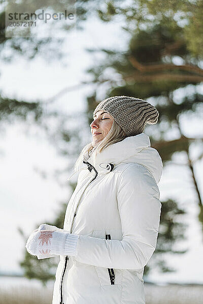 Woman in warm clothes standing with eyes closed