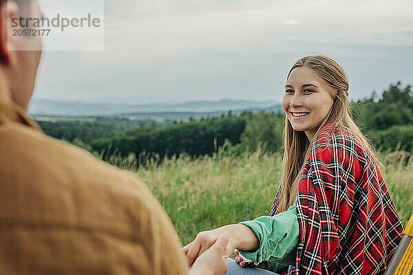 Smiling woman holding boyfriend hand and sitting on chair at mountain of Poland