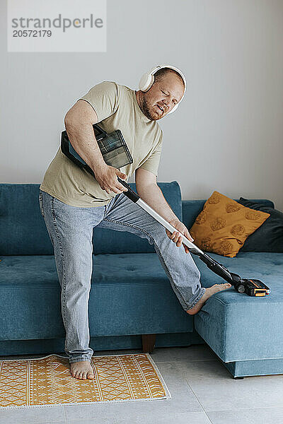 Man imitating playing guitar with vacuum cleaner near sofa at home