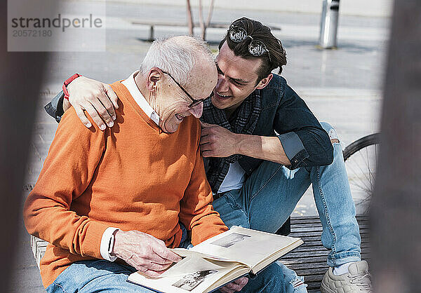 Happy grandfather and grandson sitting with photo album on sunny day