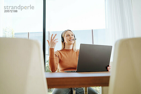 Young businesswoman talking through headset using laptop at table working from home