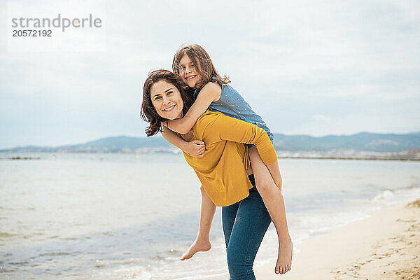 Happy mother giving piggyback ride to daughter at beach