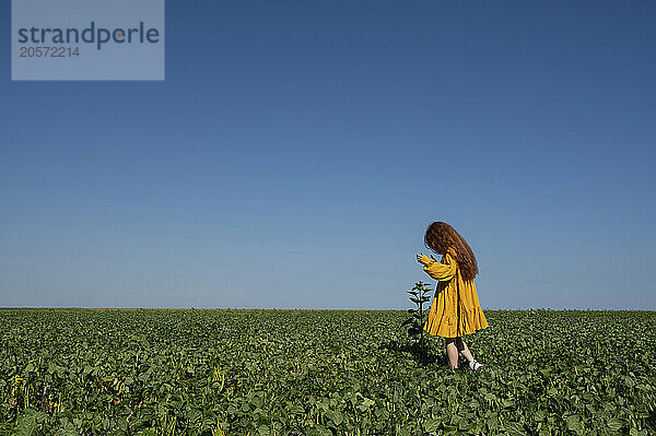 Teenage girl with red hair in a yellow dress in a green field