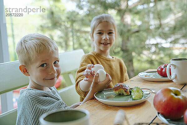 Siblings holding eggs and enjoying breakfast at farmhouse