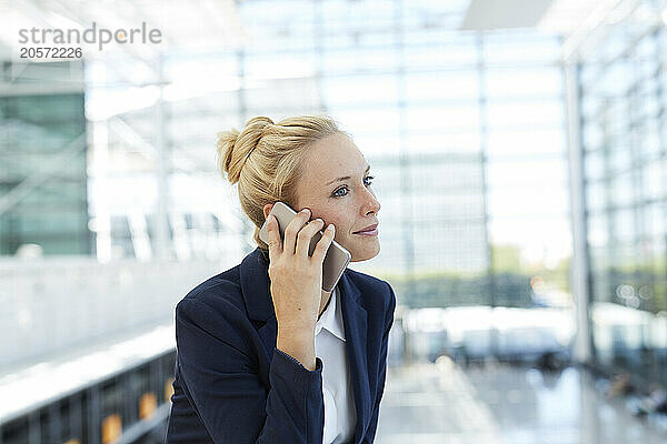 Smiling businesswoman talking on smart phone at airport lobby