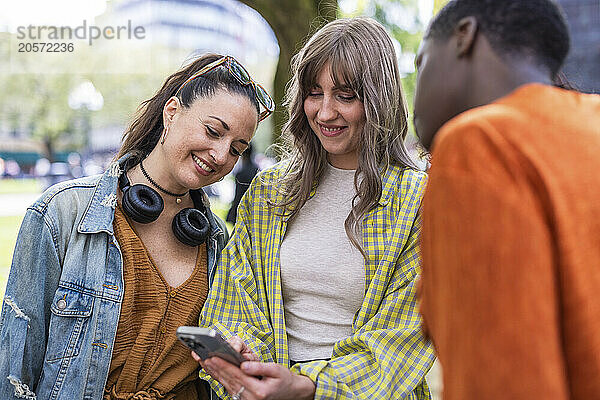 Smiling young woman sharing mobile phone with friends at park