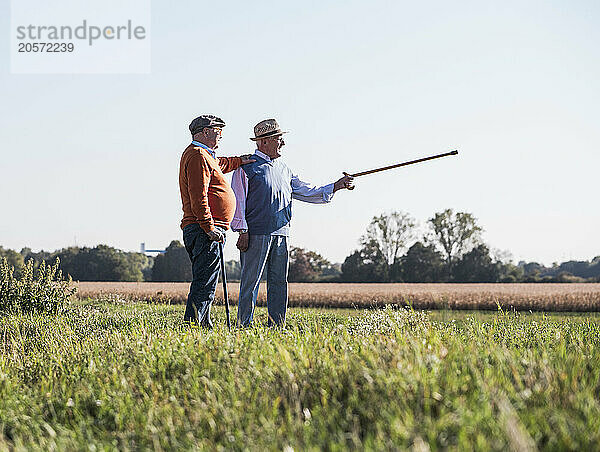 Senior man pointing direction standing with friend at field