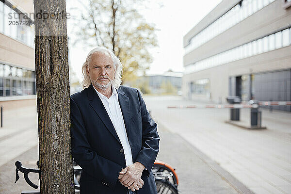 Senior businessman leaning on tree trunk at office park