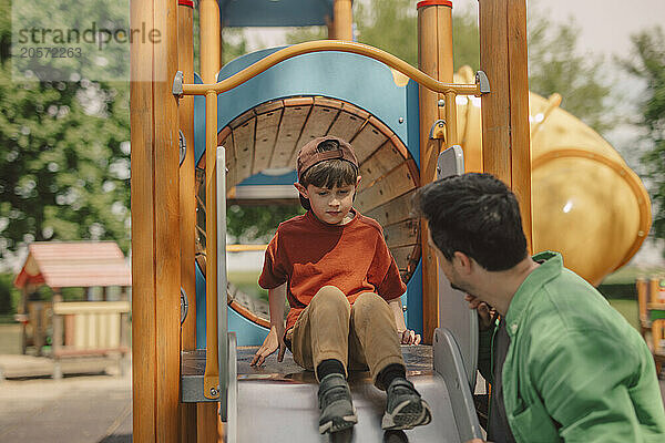 Father encouraging son to slide at playground