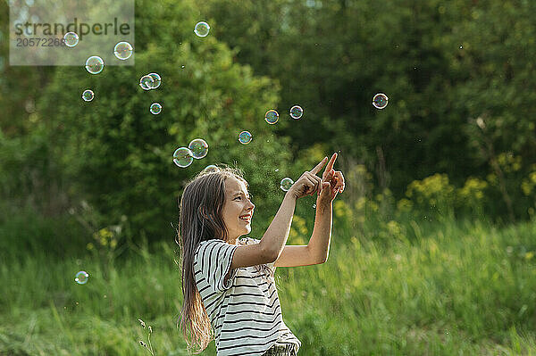 Happy girl touching soap bubbles at back yard