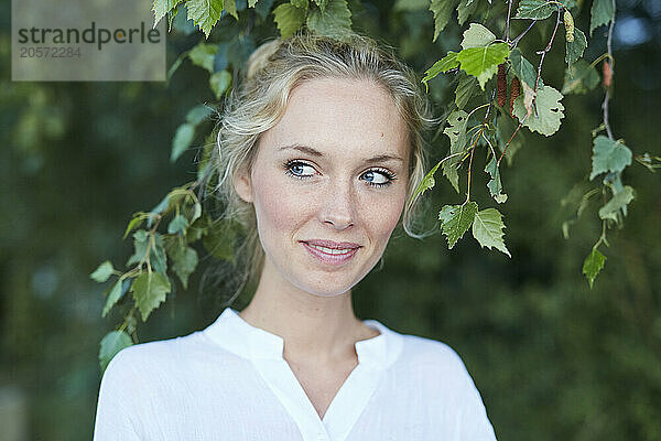 Happy blond woman standing near tree in park