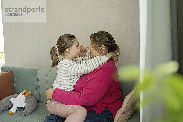 Mother and daughter spending leisure time sitting on sofa at home