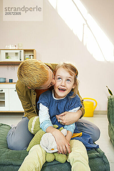 Mother kissing daughter sitting on couch at home