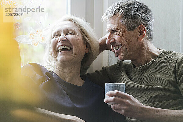 Cheerful senior couple sitting with coffee cup at home