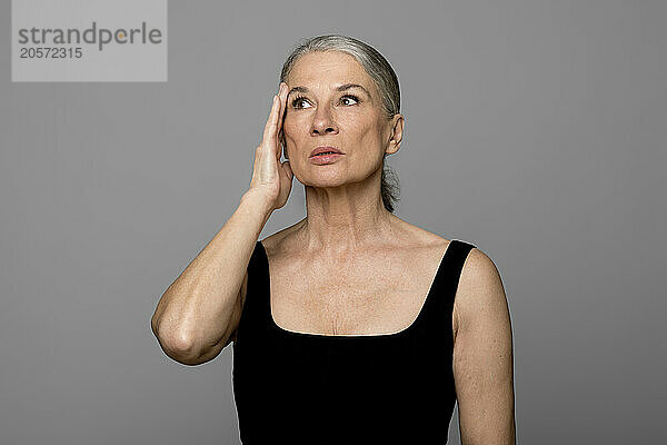 Senior woman touching head looking away against gray background