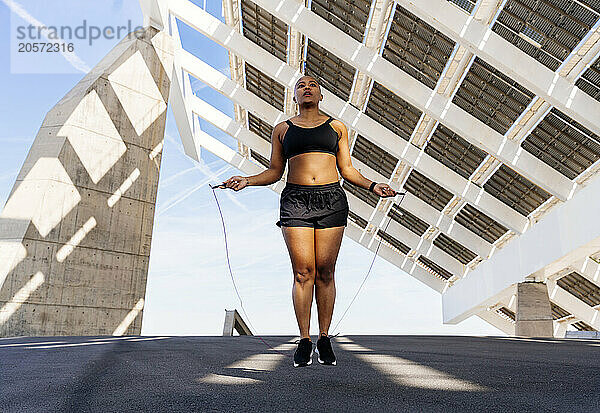 Determined sporty woman training with jumping rope on road