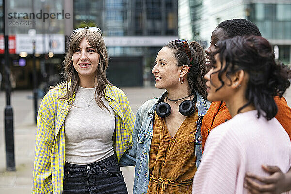 Smiling multiracial female friends standing together in city