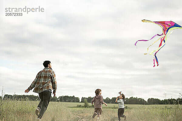 Father and sons flying kite running together on field