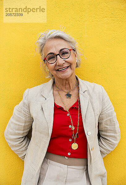 Happy elderly woman in front of yellow wall