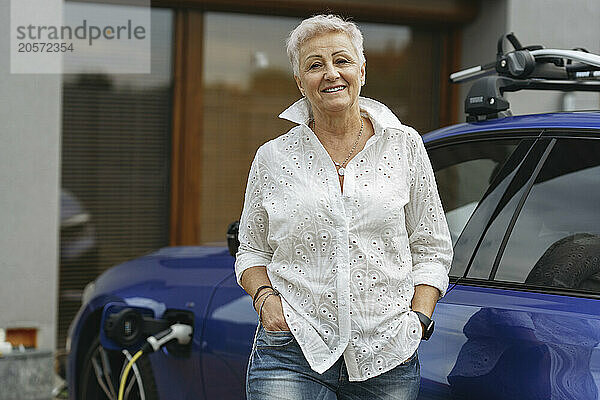 Confident senior woman in front of electric car