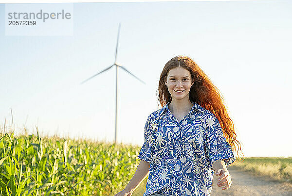 Teenage girl with red hair running in a green field and wind generators in the horizon