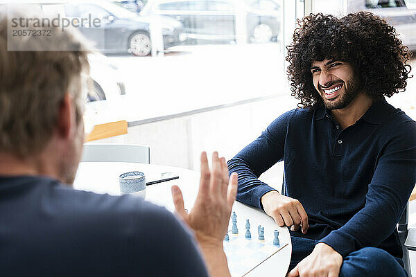 Happy young businessman playing chess with colleague at office