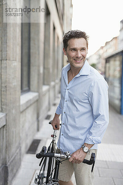 Handsome mature businessman standing with bicycle in alley