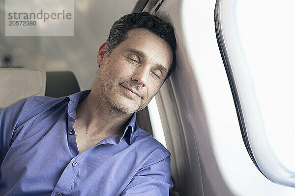 Handsome businessman leaning by window sleeping in airplane