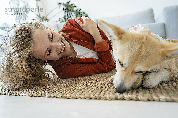 Happy woman spending leisure time with dog on carpet at home