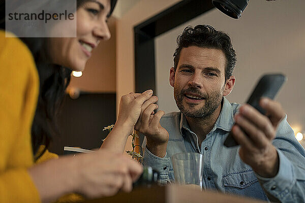 Smiling couple holding hands and using smart phone at cafe