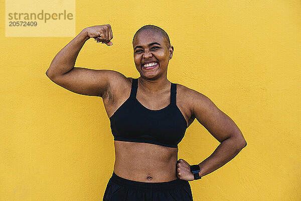 Happy muscular woman flexing muscle in front of yellow wall