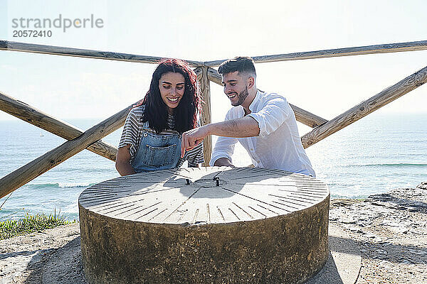 Smiling man pointing at sundial sitting with girlfriend