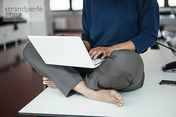 Businesswoman using laptop sitting cross-legged on conference table in office