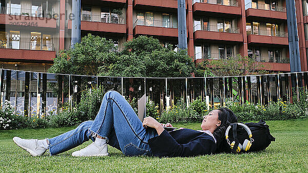 Businesswoman using laptop lying down on grass at office park