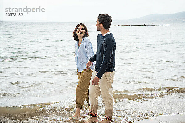 Cheerful woman walking with man in front of sea on coastline