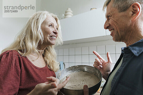 Happy retired senior couple with mixing bowl standing in kitchen at home