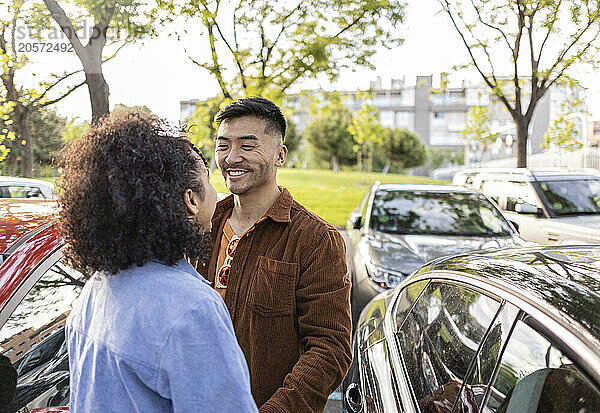 Smiling young man standing with girlfriend near car at park