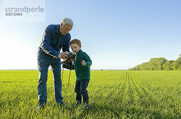 Elderly man showing his grandson old camera standing on grass