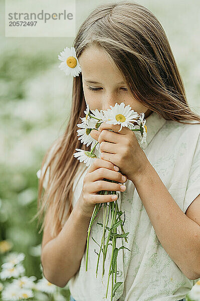 Girl smelling daisy flower in field