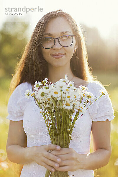 Smiling young woman holding bunch of chamomile