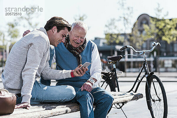 Happy man teaching smart phone to grandfather on sunny day