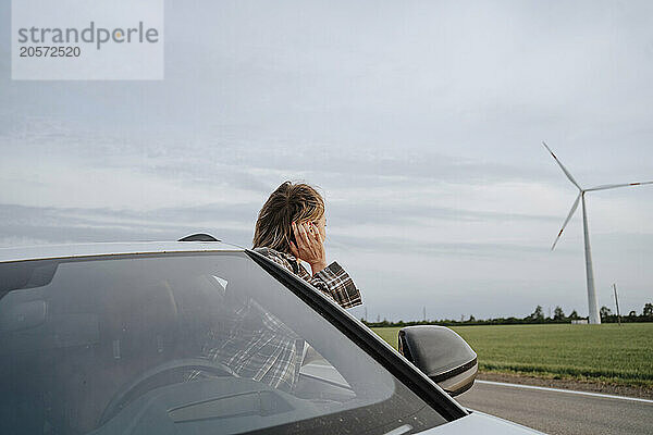 Woman leaning out of car window near wind farm