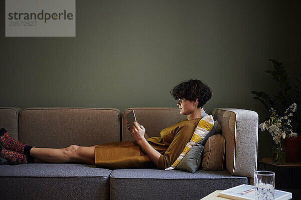 Woman relaxing and using tablet PC on sofa at home