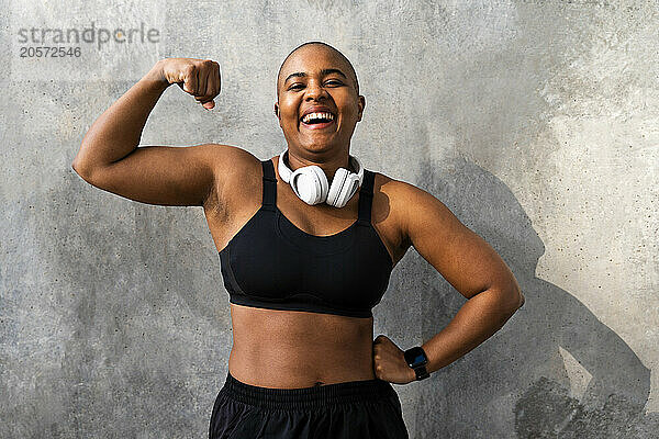 Cheerful sporty woman flexing muscles in front of wall