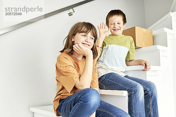 Smiling brother and sister sitting with cardboard box on staircase