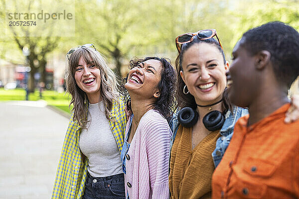 Cheerful multiracial female friends standing with arms around