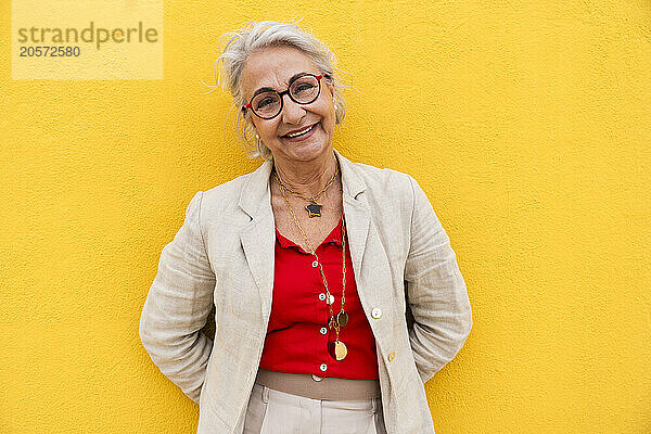 Happy senior woman leaning on yellow wall