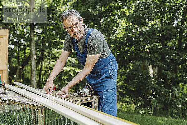 Confident mature man measuring plank with tape at back yard